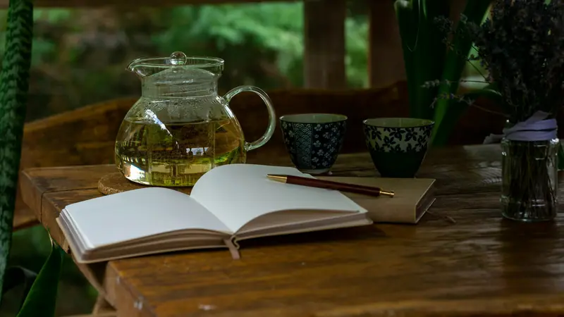 Eine Teekanne, zwei Becher und ein offenes Notizbuch auf einem Holztisch
